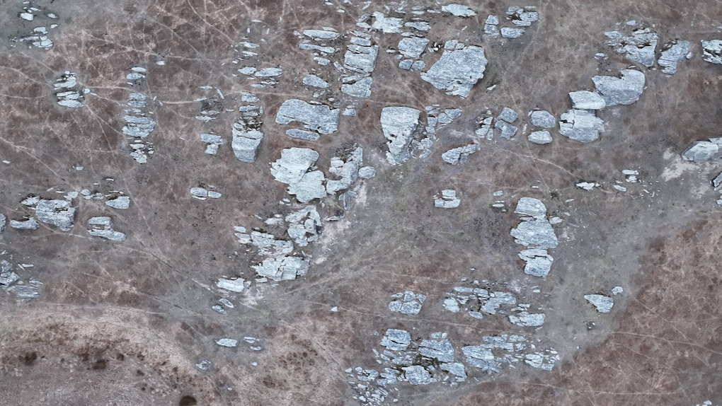 Film still from drone footage of a rocky outcrop in natural hues