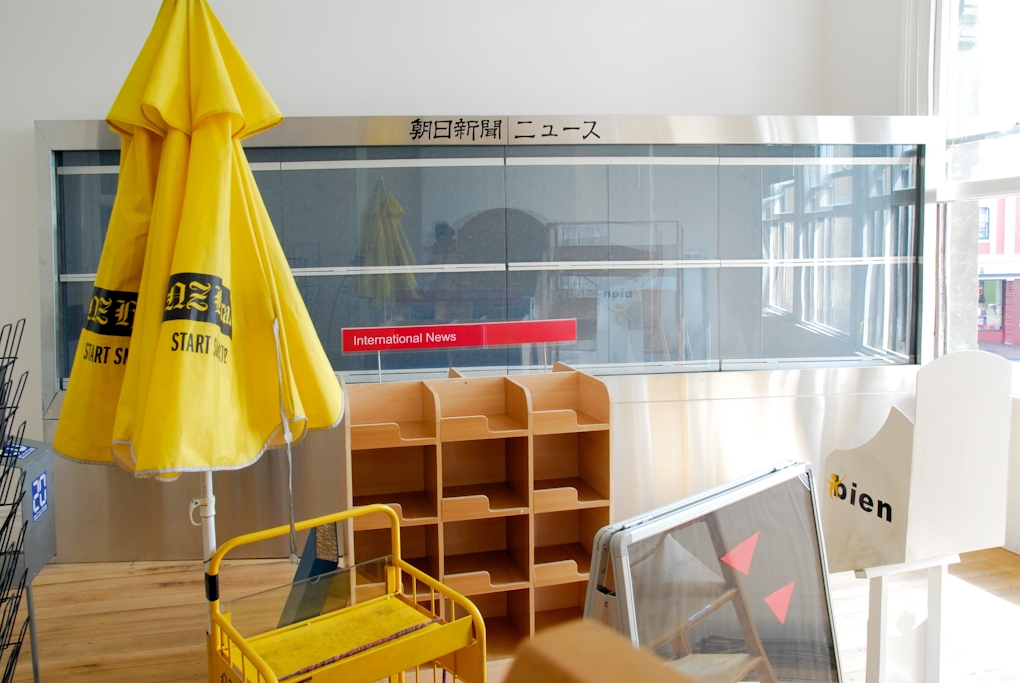Photograph of empty newspaper display shelves and umbrella with branding for the New Zealand Herald newspaper.