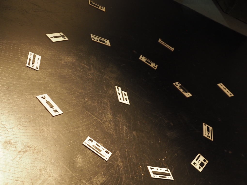 A series of graphic scores lie on the floor in a circle. Each score is made of leather cut outs stuck on top of rectangular cards.
