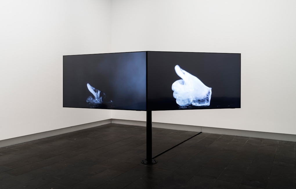 A two screen video installation, showing at right, a hand made of ice giving the thumbs up gesture, and at left, the same image melting.
