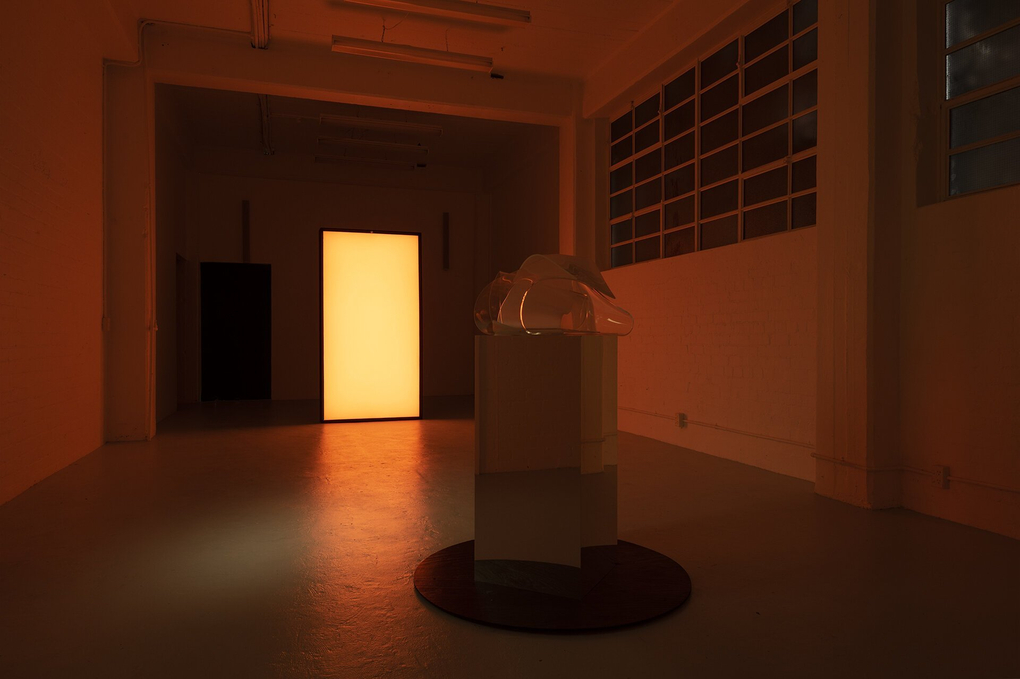 A plastic object on a plinth in a dark room illuminated by a bright screen
