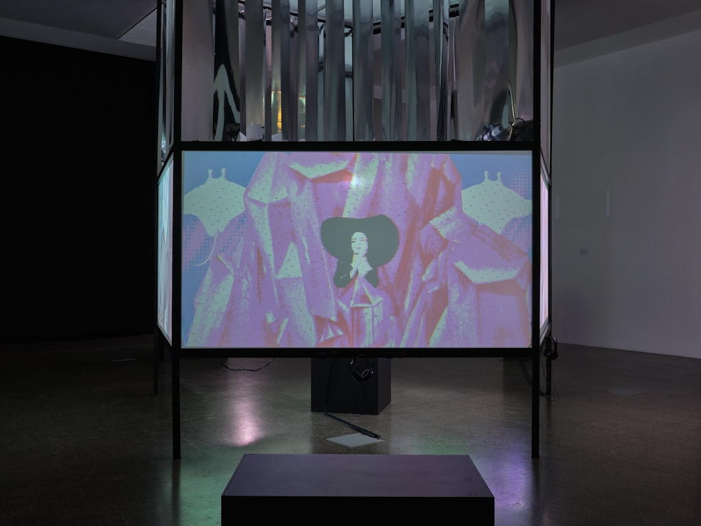 Installation view of a film screen in a darkened room. The screen is mounted on a three-sided structure.