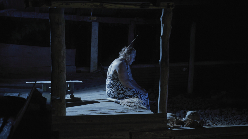 A woman sits at the edge of a fale at night