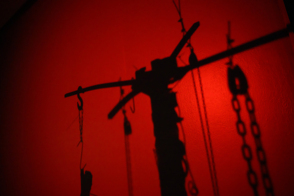 A sculpture of hooks and chains against a red wall