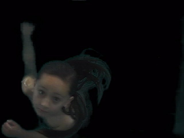 A young boy floats in the dark, looking up at the camera. His hair floats around him and his arms are outstretched.