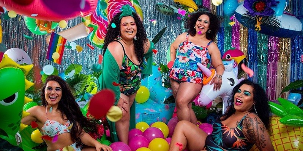 Four people laugh happiily wearing brightly coloured swimwear, in a room of blow up pool toys and sparkly decorations