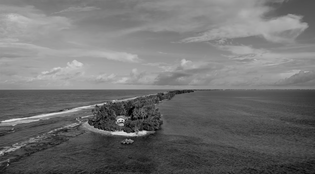 Black and white aerial footage of a Pacific island surrounded by ocean
