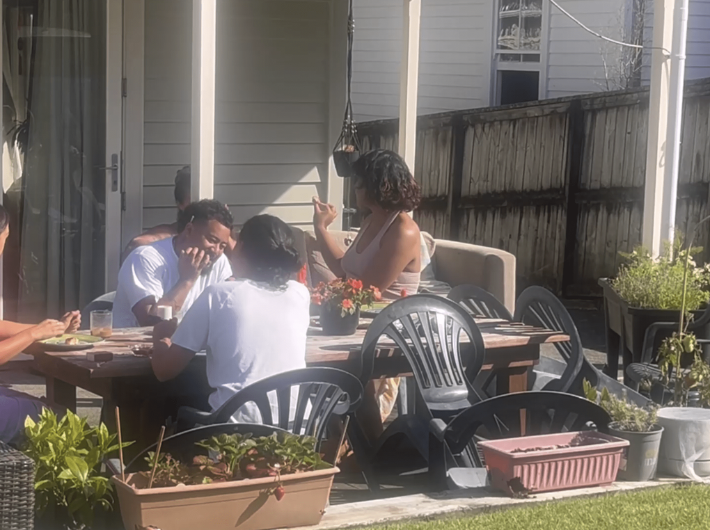 Friends hang out at a table in a sunny backyard.