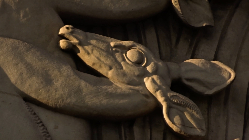 A sculpted stone head of a deer or antelope in golden sunlight