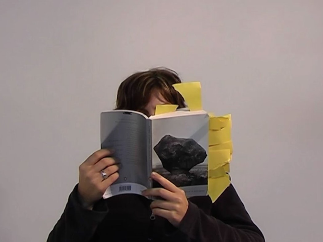 Christina is reading, holding a book which spills with bookmarks, very close to their face