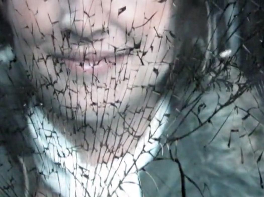 The image of a person's face behind a cracked screen.