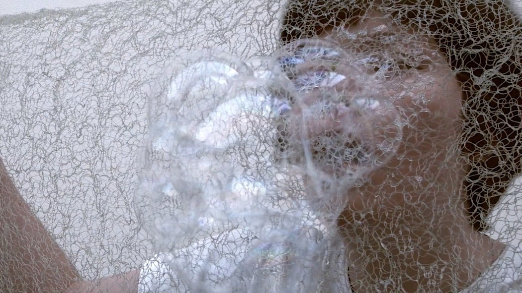 A person blows bubbles through mesh fabric.