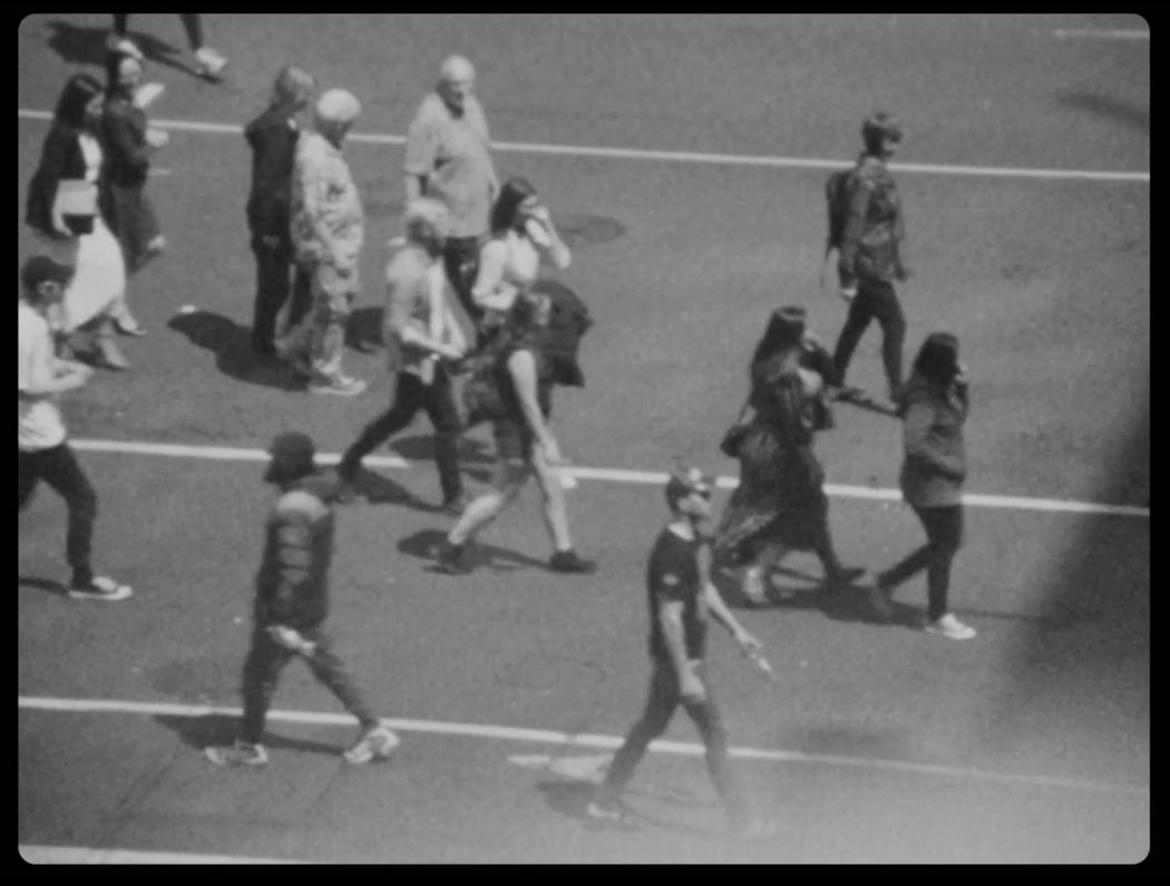 A grainy black and white image of pedestrians crossing an intersection.