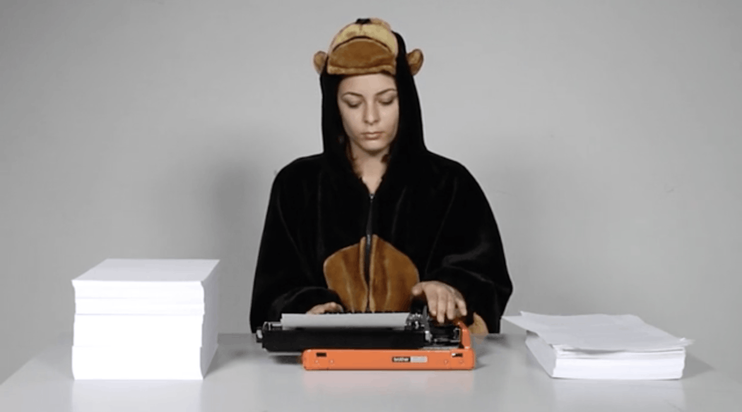 A person wearing a monkey onesie types on a orange type writer.
