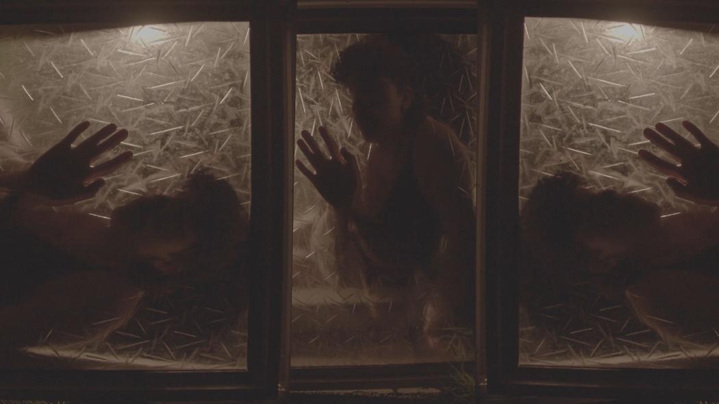 Behind three panels of frosted glass we see three separate shots of the same person with their hand pressed to the glass. Their face is in shadow.
