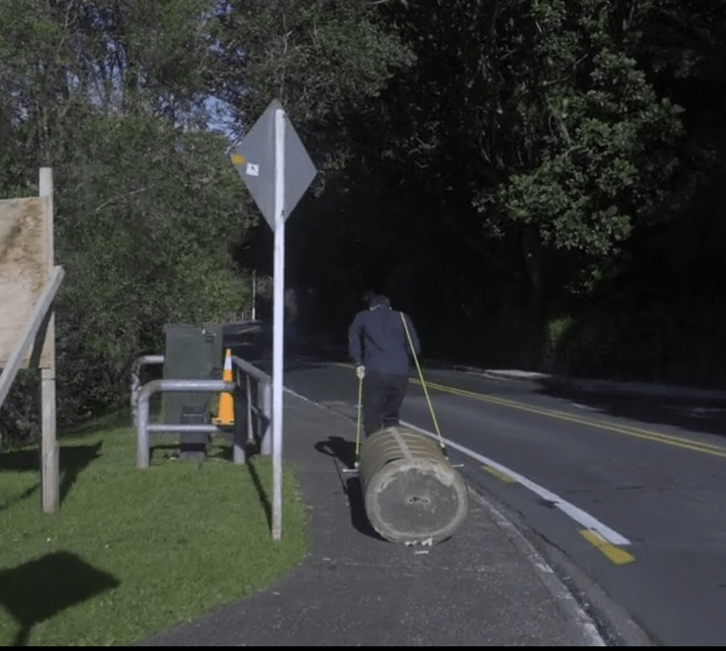Mark is dragging a huge log on a footpath on a suburban street