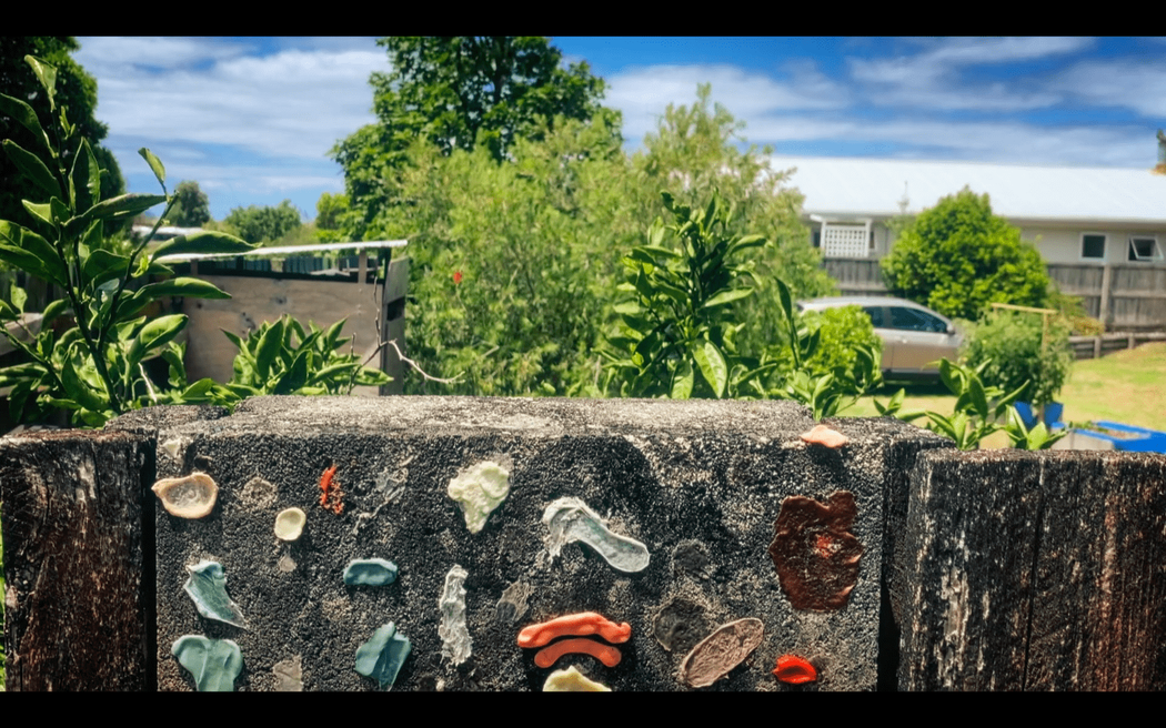 Colourful bits of chewing gum are affixed to the concrete of a suburban fence