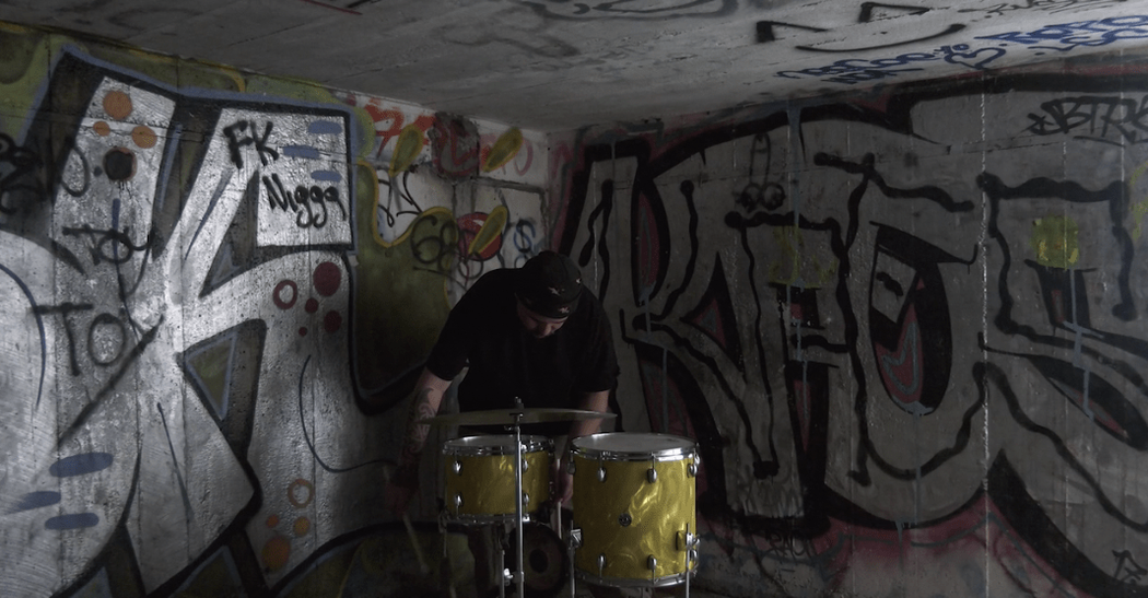 A man in a graffitti'ed concrete bunker plays the drums