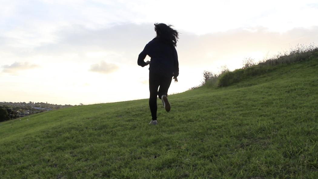 A black silhouette of a person running towards the top of a hill in late afternoon pale winter light.