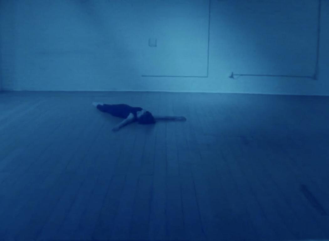 In a blue light, a dancer lies on the floor of a dance studio