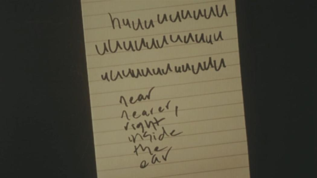 scrawled text on a notepad which begins with three lines spelling 'huuuuu...' and ends with 'near, nearer, right inside the ear'.