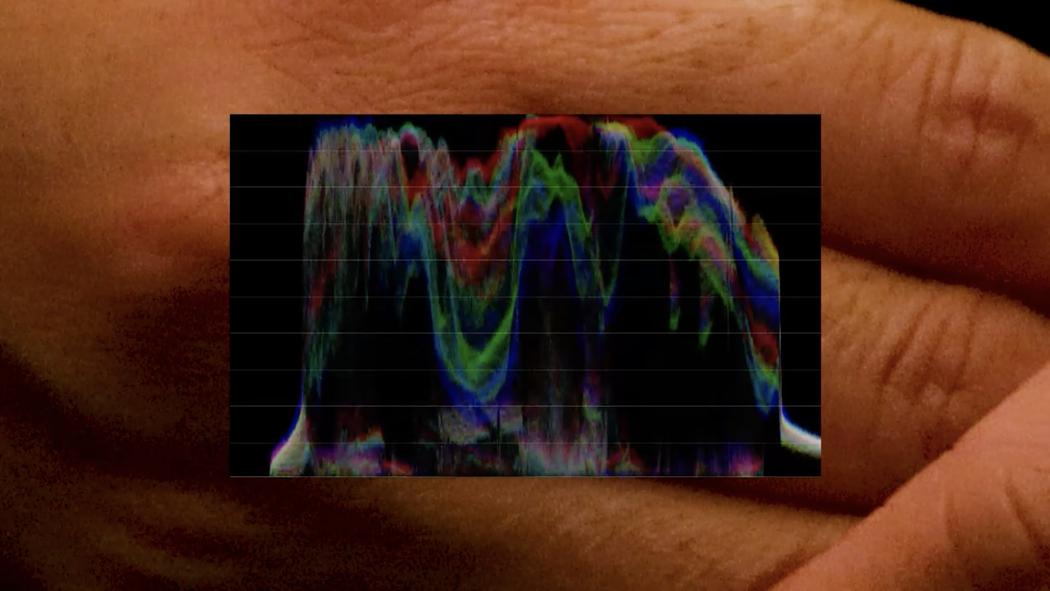 Over a close up image of fingers we see a colourful spectral wave form.
