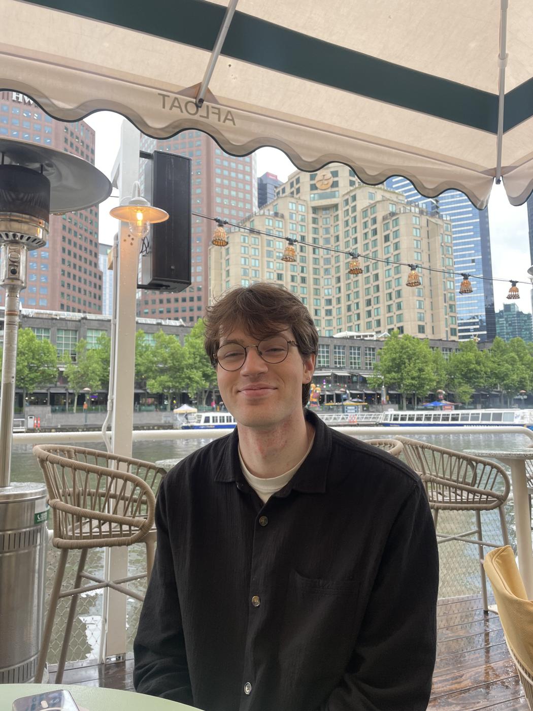 A person sits smiling in a bar, beside a canal