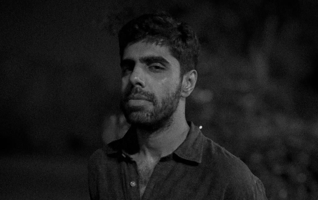 In dark moody light a person looks unexpressively at the camera