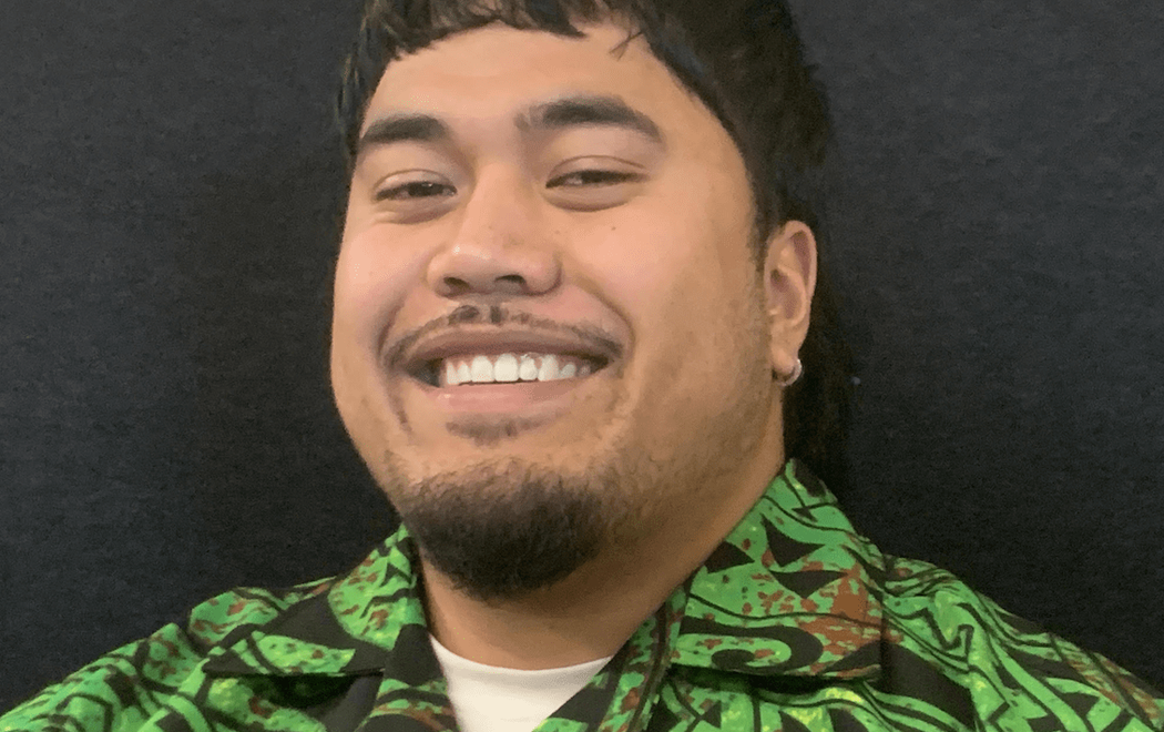 A man smiles at the camera, he is wearing a bright green shirt