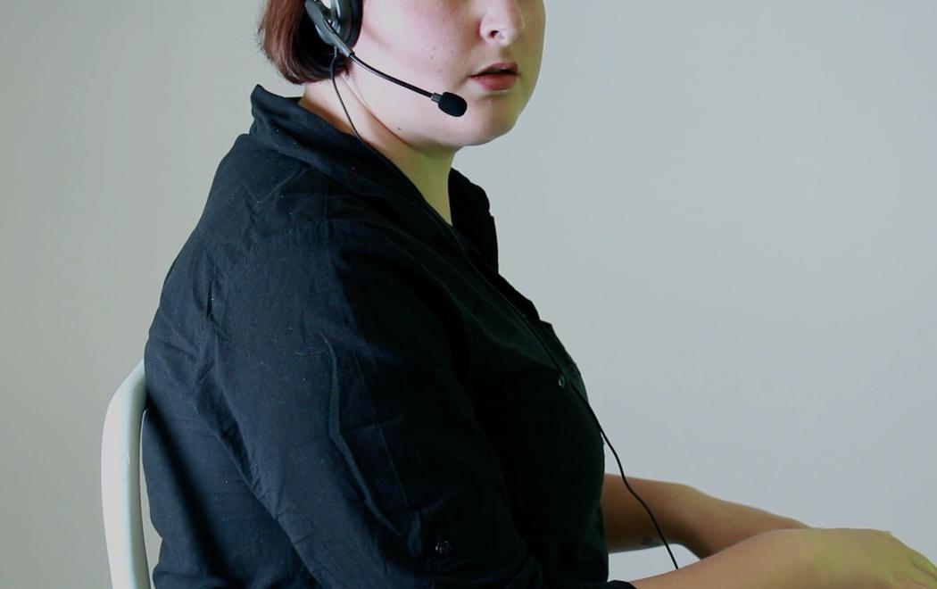 A person wearing a call centre headset and appearing to type at a keyboard turns their head to the right, as if suddenly having their attention drawn elsewhere.