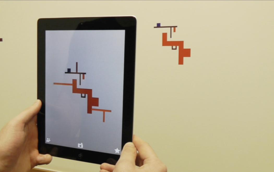 A person holds up a tablet in front of a geometric shape on the wall. Through the video screen the geometric shape is embellished with extra design elements