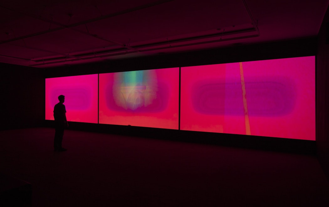 Three bright pink screens in a darkened gallery
