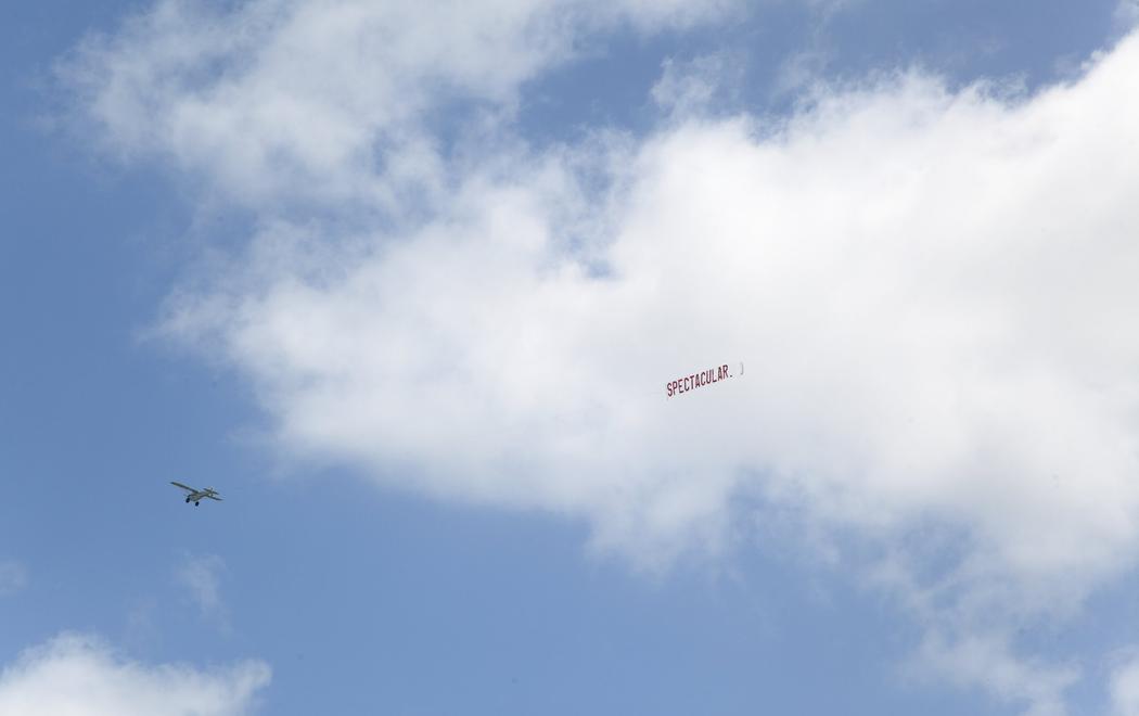 A plane flying in the blue skies toes a banner with the word SPECTACULAR in large red text