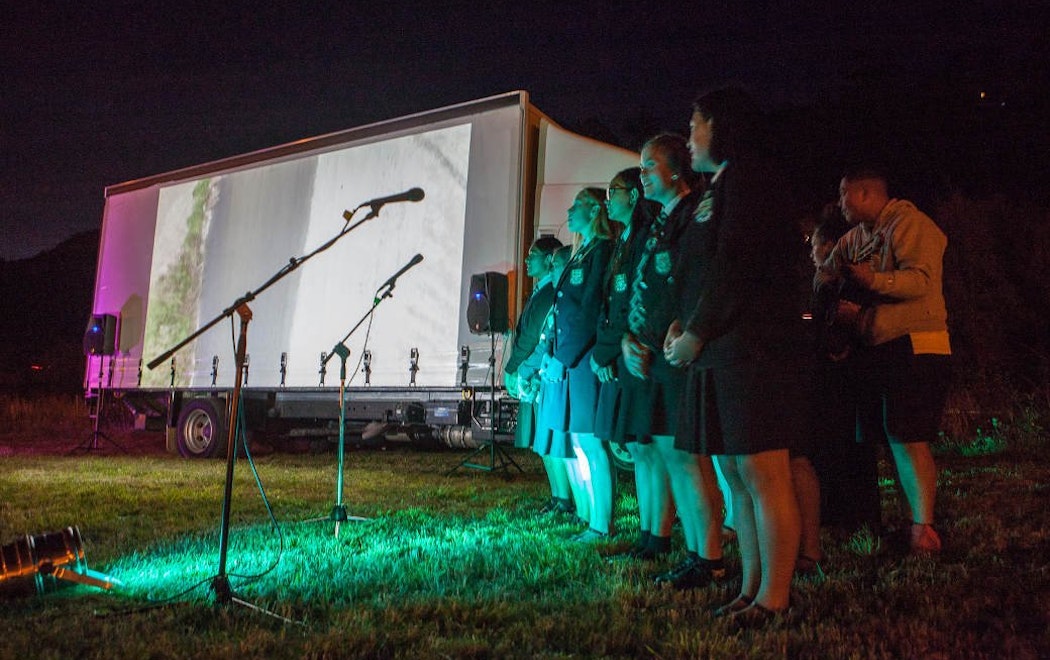 A group og high school students sing in front of an image projected on a truck