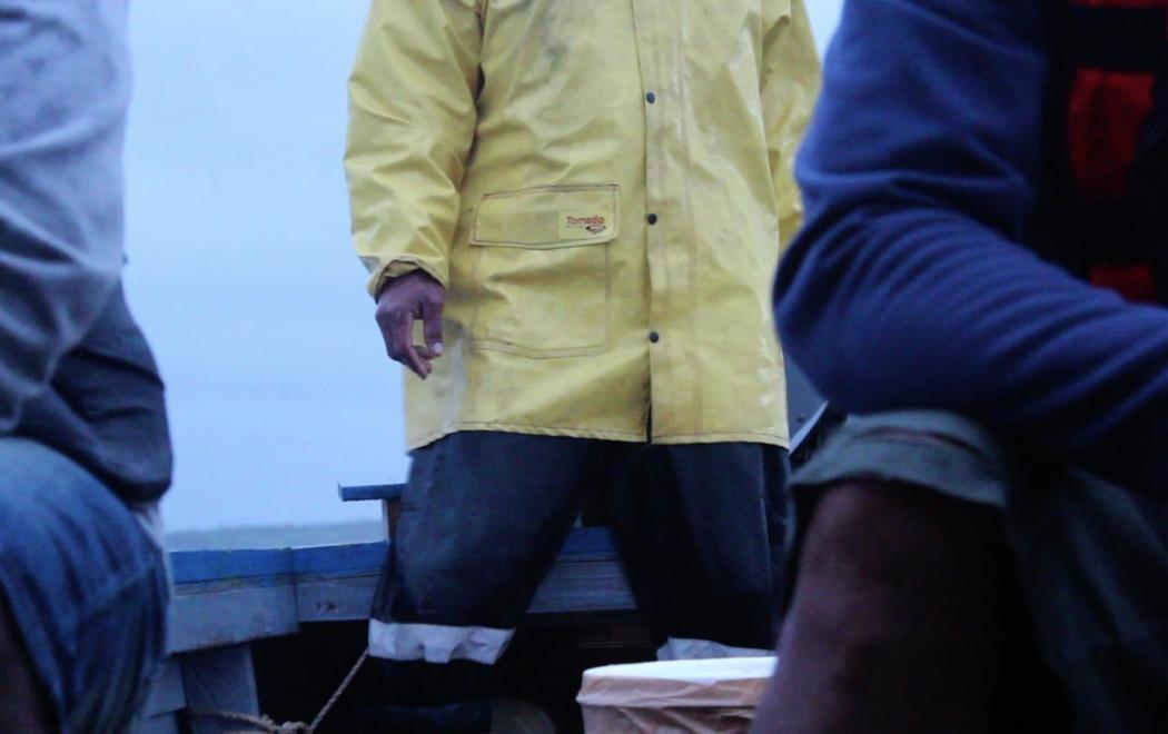 A sailor wearing oilskins stands in the stern of a small boat