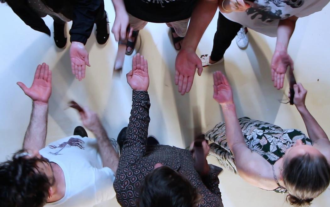 Six people play a musical game, hitting each other with leather belts whilst facing each other