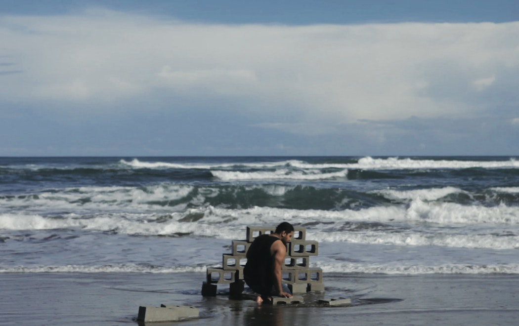 A person builds a wall from concrete bricks on the wet sand as the waves crash near by