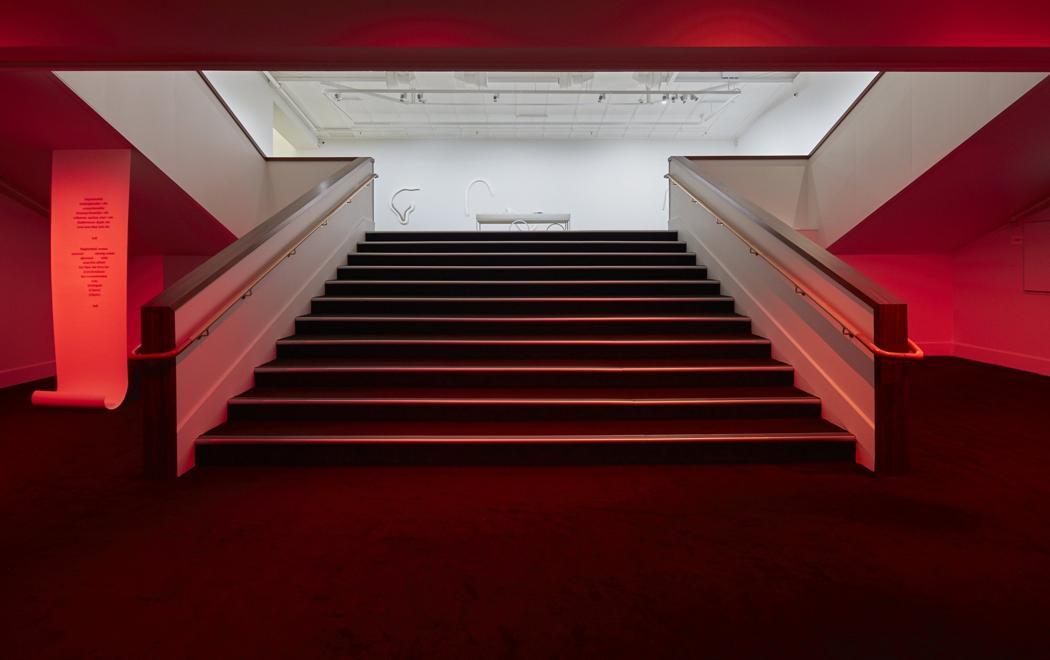 A classic cinema staircase is bathed in red light, at left a scroll of paper hangs down