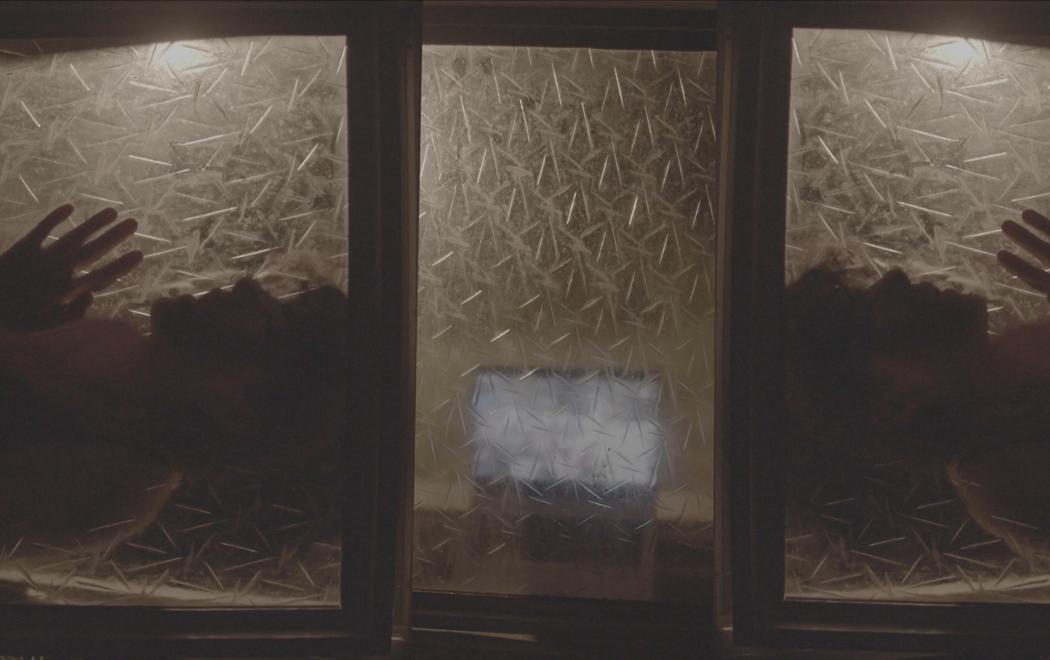 Three frosted windows are lit up from behind by lamps. One on each side reveal the silhouette of someone caressing the window, while the middle window shows a laptop playing a video.