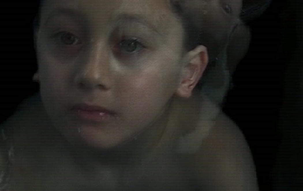 A close-up of a young boy swimming in the dark, staring up at the camera. Another image of him is superimposed, his arms outspread.