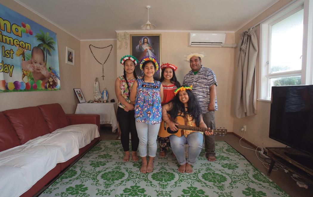 Four people stand together in a colourful lounge smiling brightly wearing pasifika headdress