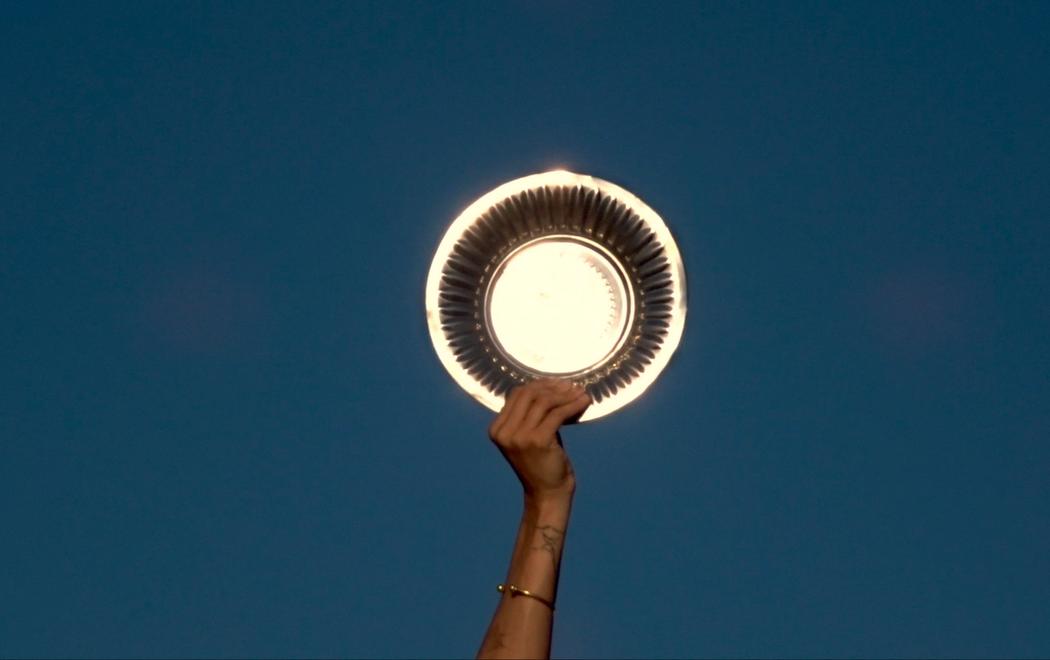 A hand holds a gold charger plate up against a bright blue sky