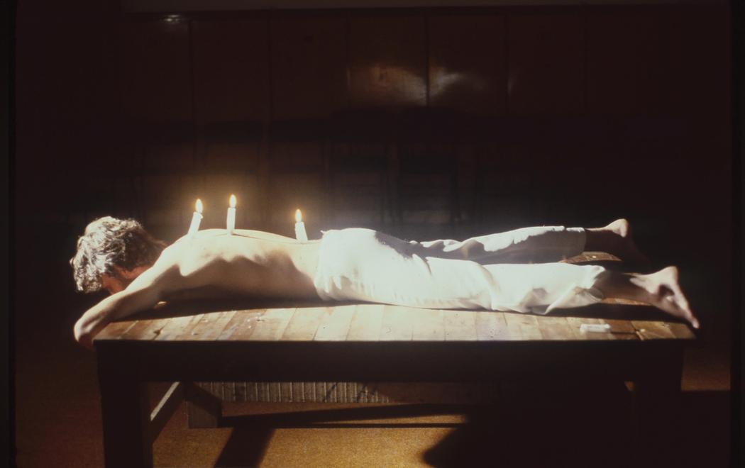 A man lies on a table with three burning candles mounted on his back