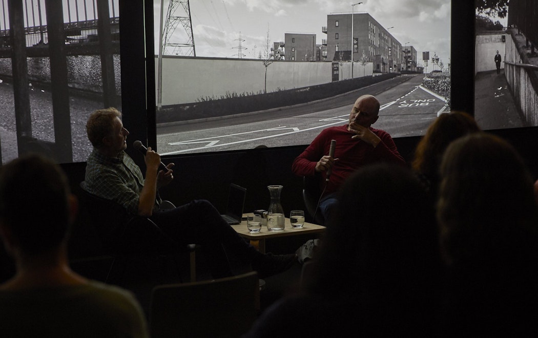 Mark Williams and Peter Wareing sit in front of three large screens displaying Peter's work in conversation.