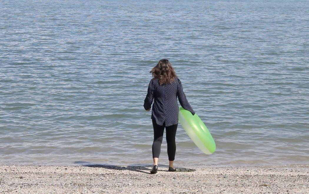 A person in retail working clothes holding an inflatable ring and walks towards the ocean.