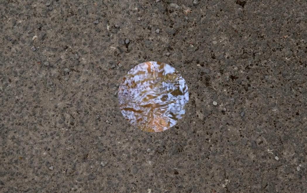In a concrete wall we see a circle which shows a watery reflective surface.