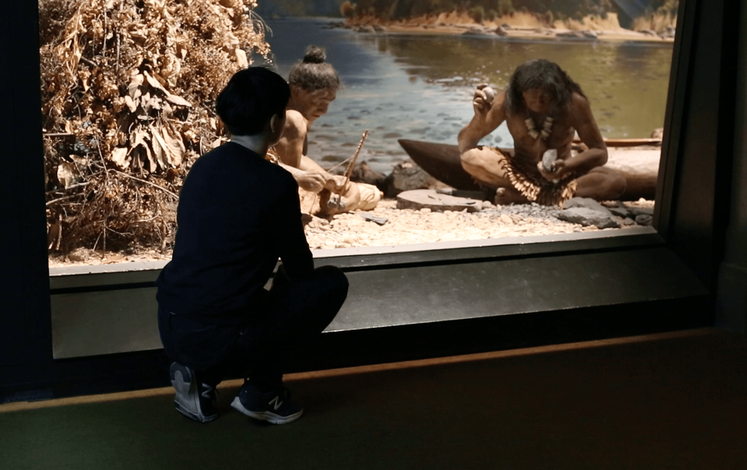 Ana squats down in a museum to haze upon a racist exhibit of Māori people in a museum