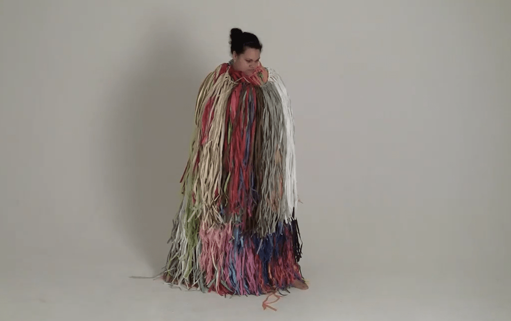 Darcel stands in a white raffia costume against a plain white background