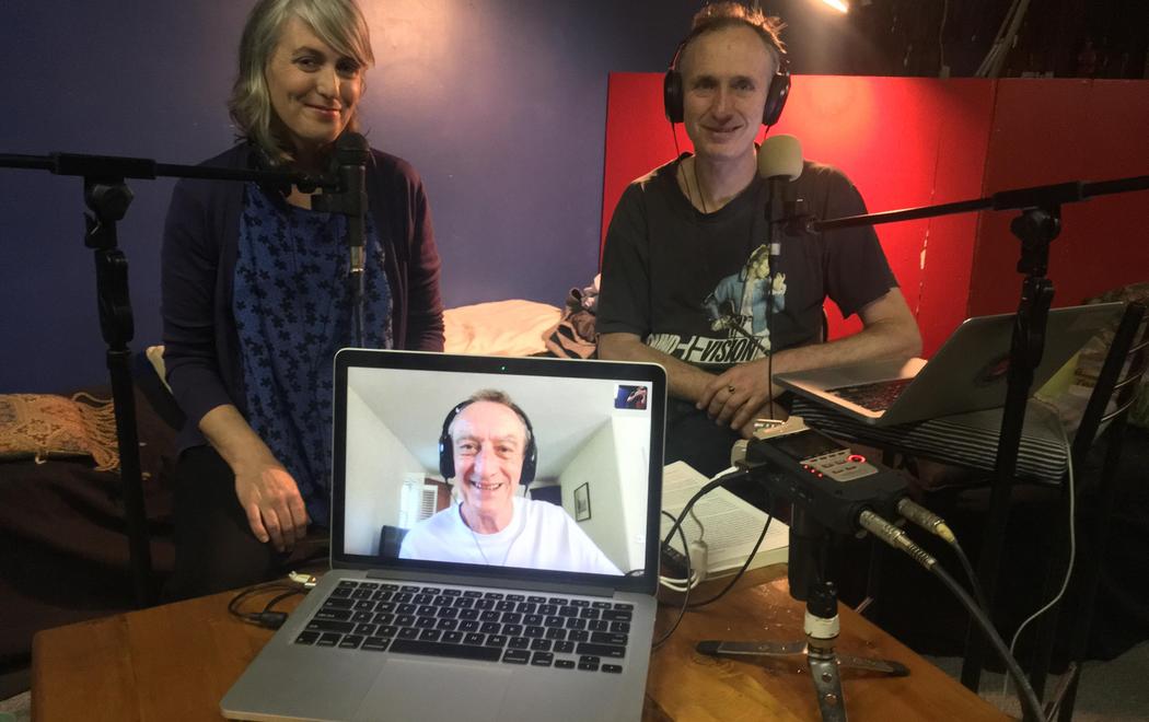 Stella Brennan and Mark Amergy smile in a audio studio holding a laptop showing Sean Cubitt smiling