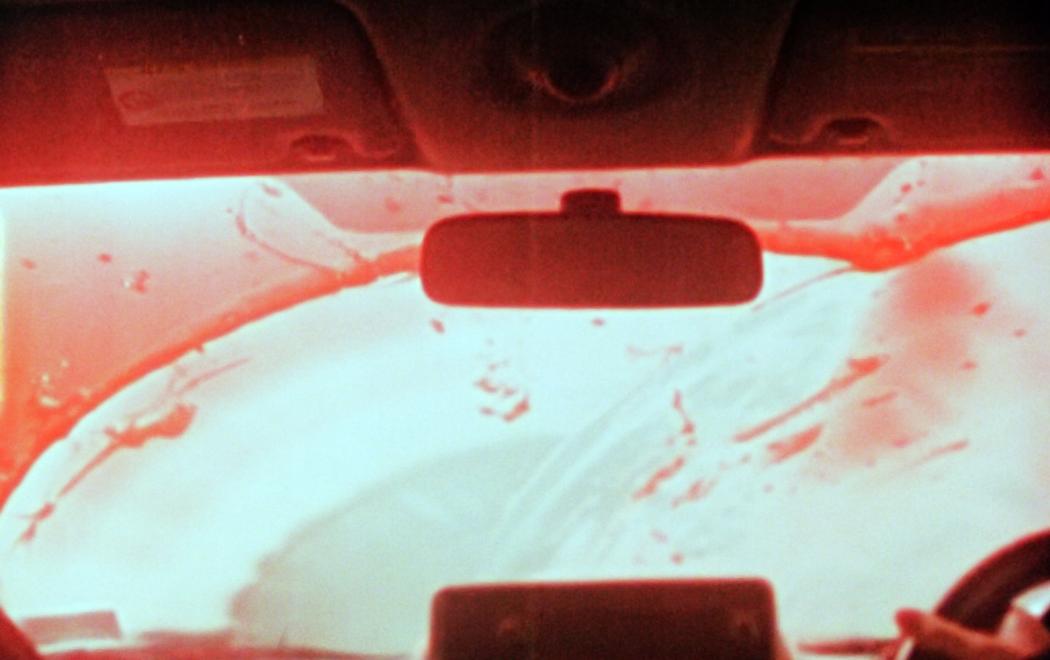 Red liquid or blood is wiped from a car windscreen, seen from inside the car